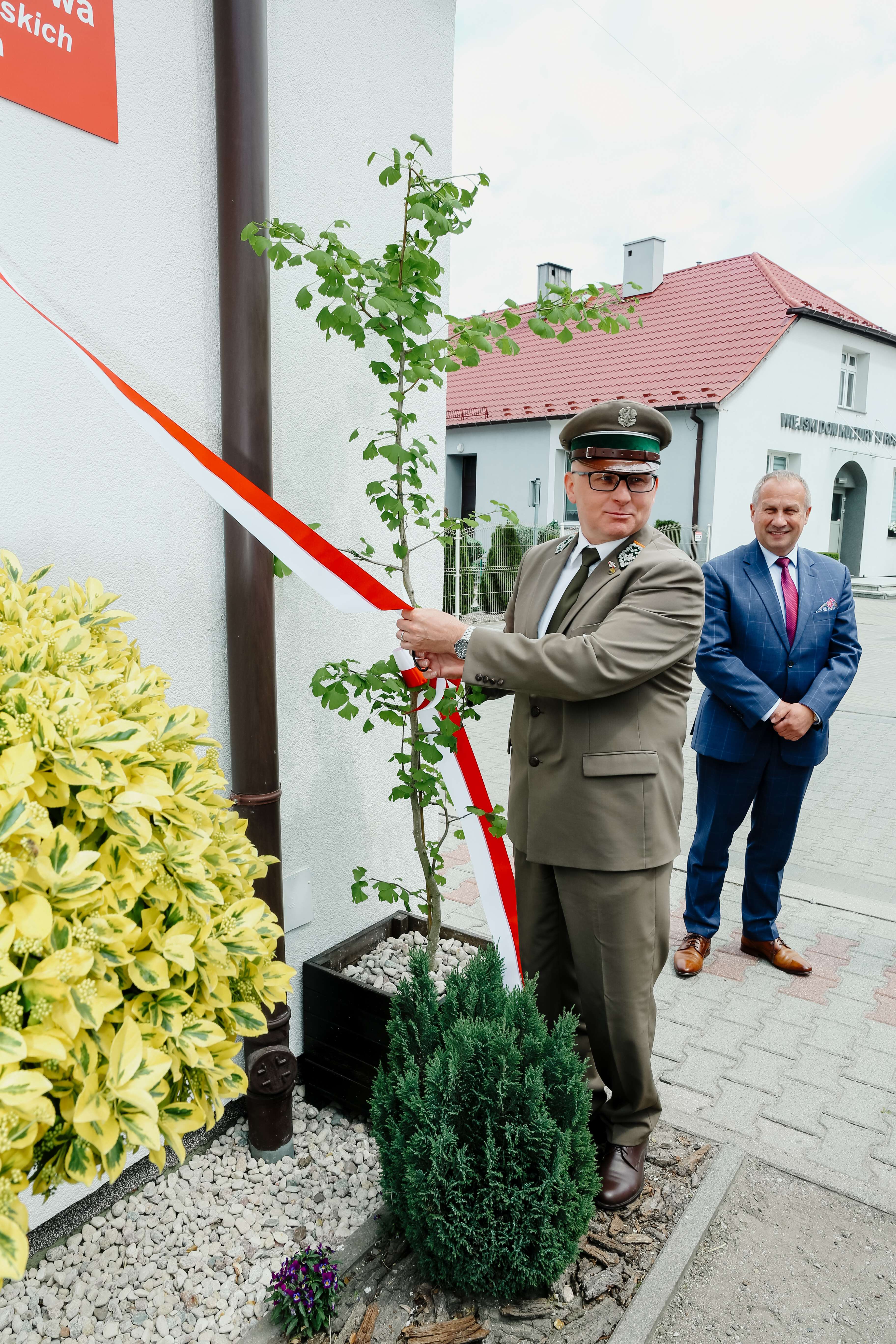 Zdjęcie przedstawia dyrektora Andrzeja Koniecznego trzymającego wstęgę w polskich barwach przy tablicy z nowym imieniem szkoły. Źródło: Archiwum SP w Roszkach. 