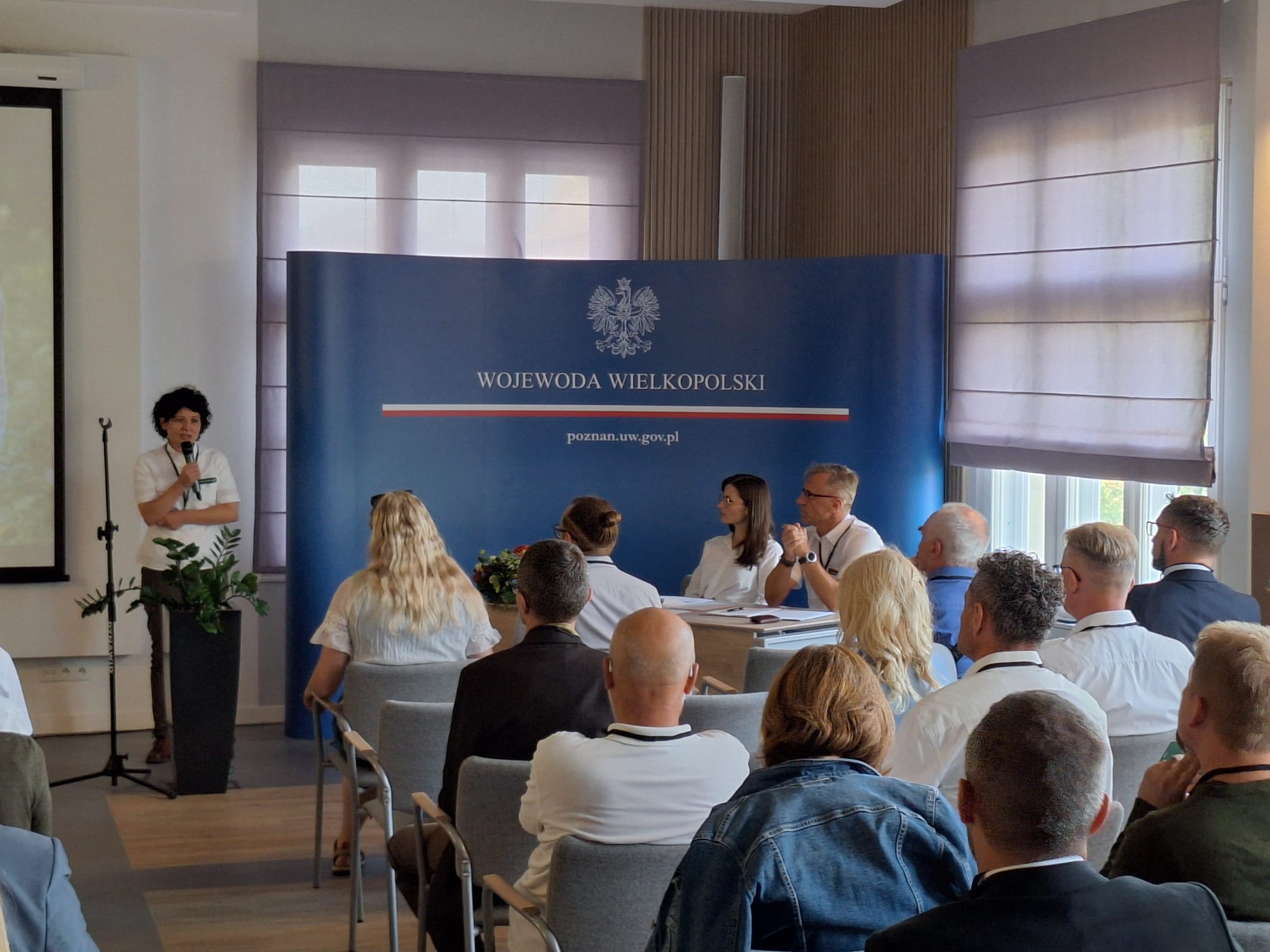 Zdjęcie przedstawia zgromadzonych na sali członków Zespołu, jedna z członkiń stoi z mikrofonem frontem do zgromadzonych, po prawej za stołem dyrektor RDLP w Poznaniu i Wojewoda Wielkopolska. Fot. Wojciech Fabisiak