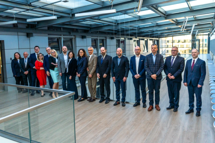 Grupa kilkunastu kobiet i mężczyzn w oficjalnych strojach, w tym dyrektor RDLP w zielonym mundurze, stojących w przejściu nowoczesnego, przeszklonego budynku. Fot. Sieć Badawcza Łukasiewicz - Poznański Instytut Technologiczny